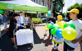 Dwie osoby kroją tort, z boku dwie osoby z balonami